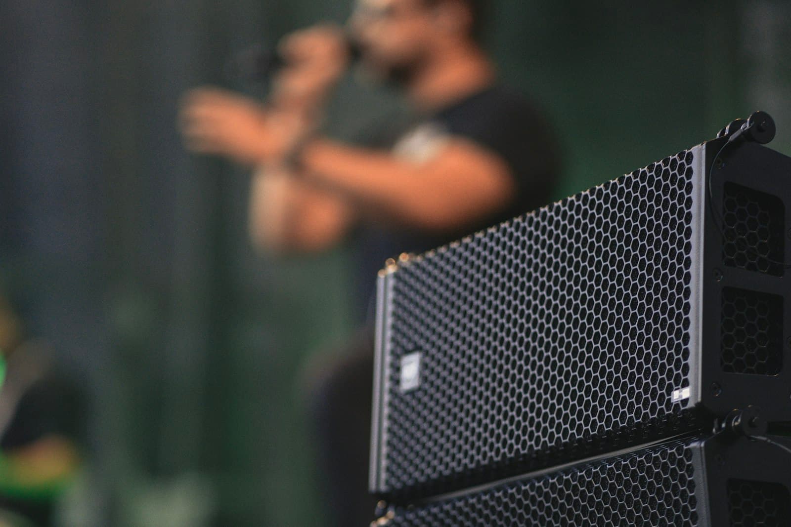 Line-Array-Lautsprecher im Vordergrund, dahinter ein Sänger mit Mikrofon auf der Bühne